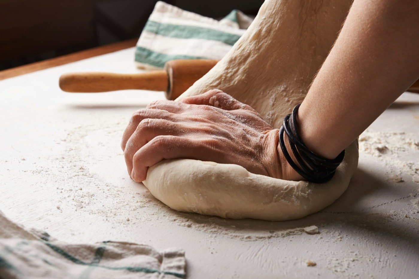 Hands kneading bread dough on a floured surface next to a rolling pin