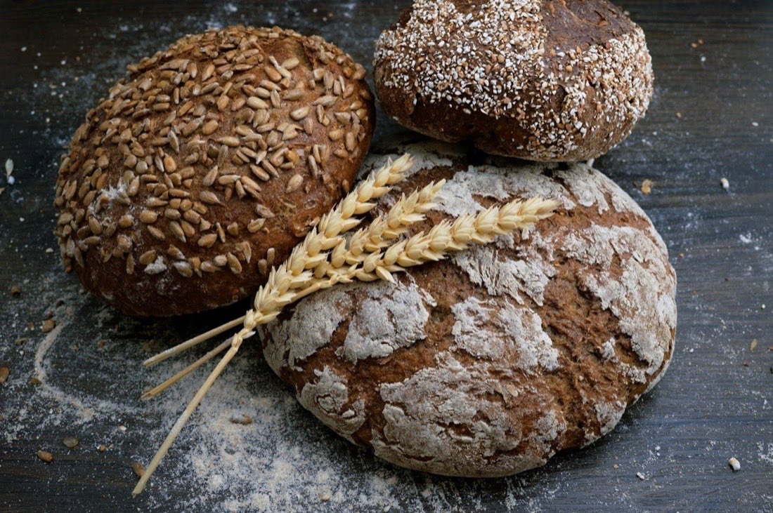 Three rustic seeded bread loaves dusted with flour on a dark wooden surface