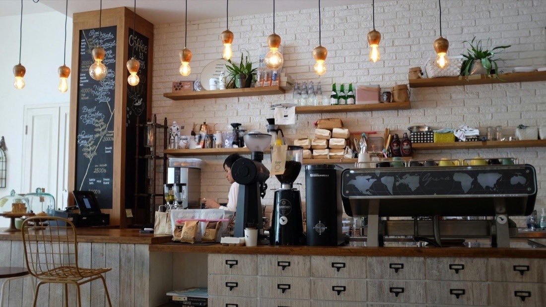 A cafe counter with an espresso machine, hanging lights and a white brick wall