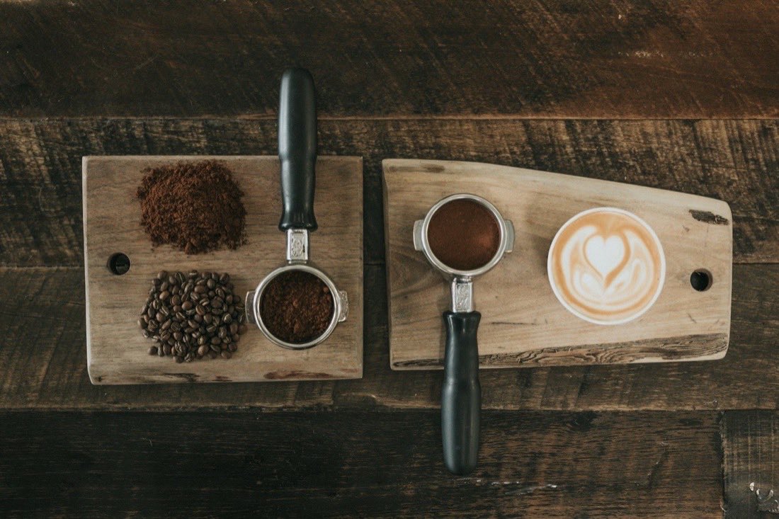 Two espresso portafilters with ground coffee and beans on wooden boards