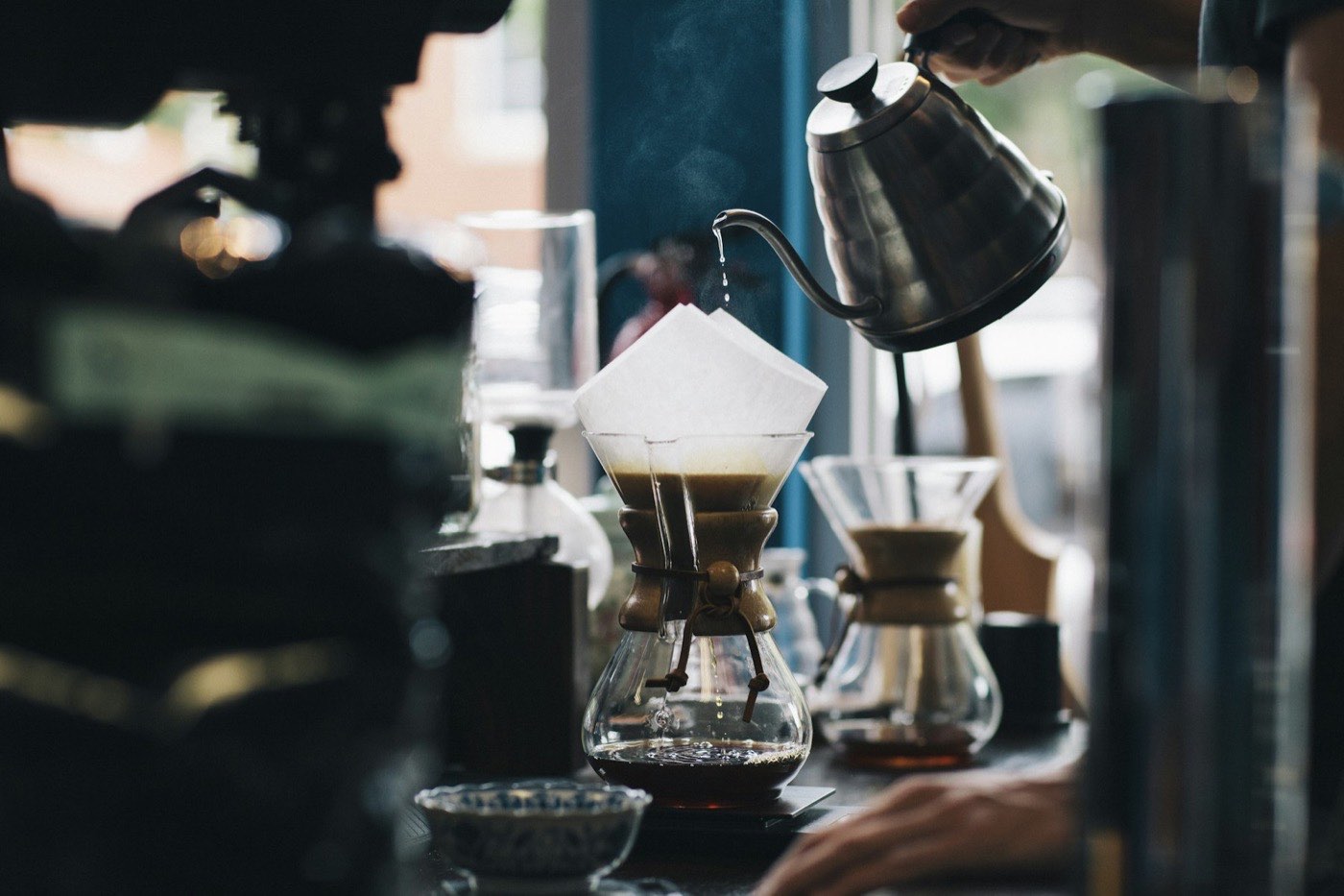 Hot water being poured from a gooseneck kettle into a glass pour-over brewer