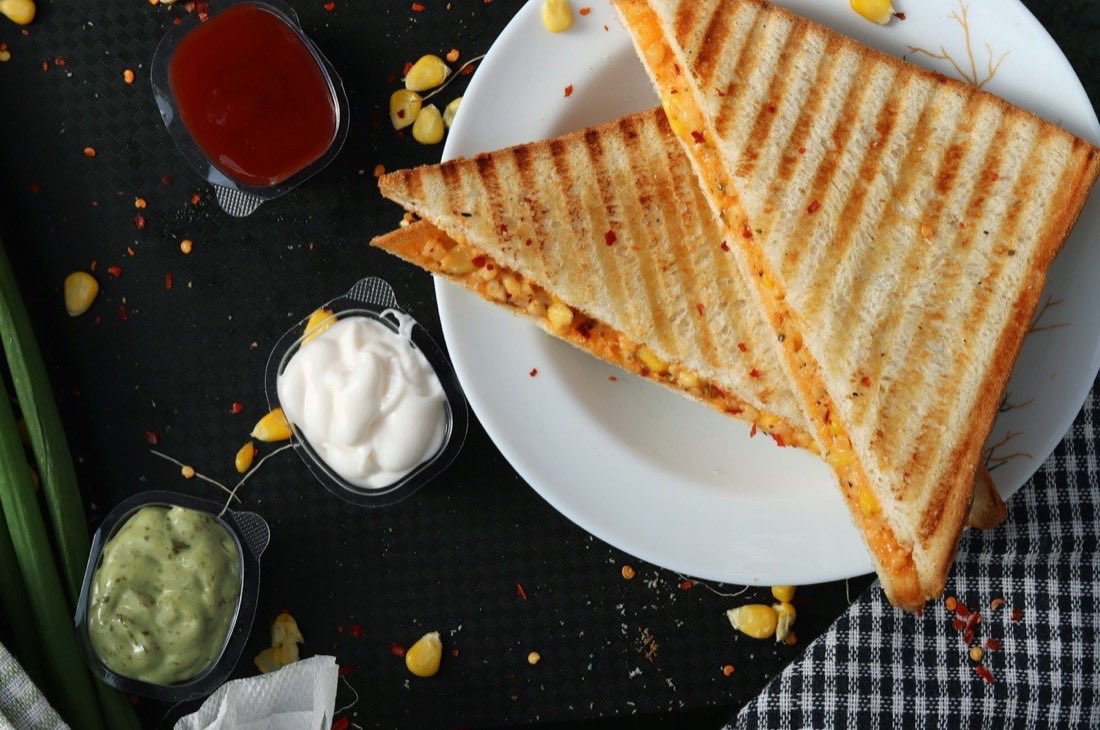 A toasted sandwich cut in half on a white plate with dipping sauces