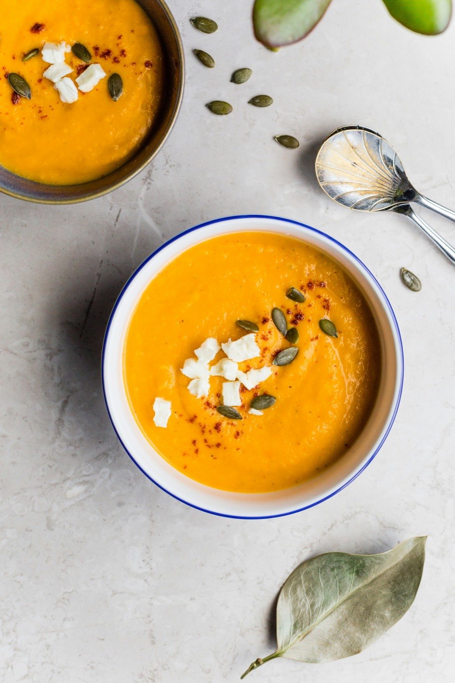 Two bowls of thick squash soup topped with seeds and cheese